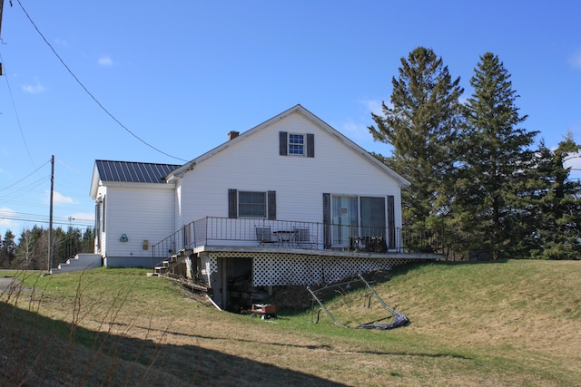 rear view of property featuring a lawn, a wooden deck, and metal roof