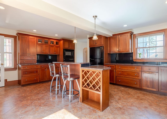 kitchen featuring a breakfast bar area, brown cabinetry, a center island, backsplash, and black appliances