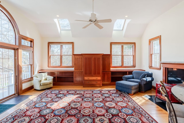 living area featuring ceiling fan, vaulted ceiling with skylight, and light wood-type flooring