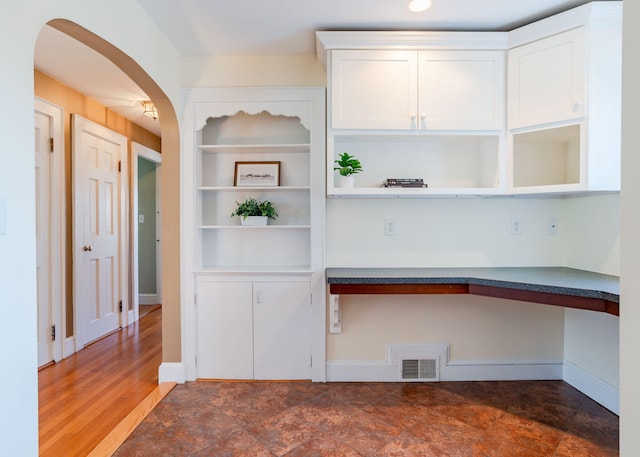 interior space with built in study area, arched walkways, baseboards, and visible vents