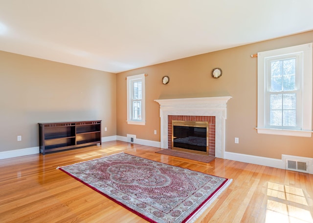 living area with visible vents, baseboards, a brick fireplace, and wood finished floors