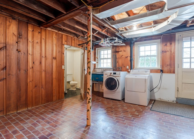 washroom with brick floor, laundry area, wood walls, and independent washer and dryer