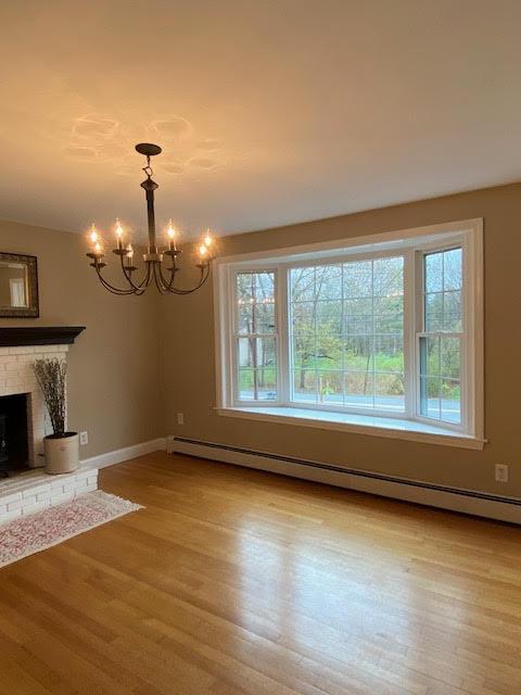 unfurnished living room with an inviting chandelier, light wood finished floors, a baseboard heating unit, and a healthy amount of sunlight