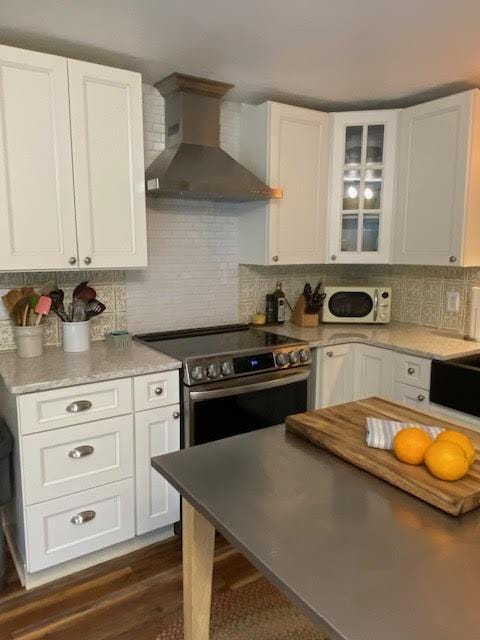 kitchen featuring stainless steel electric stove, white cabinets, white microwave, and wall chimney exhaust hood