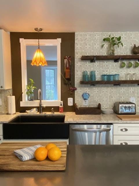 kitchen with decorative light fixtures, tasteful backsplash, stainless steel dishwasher, a sink, and white cabinets