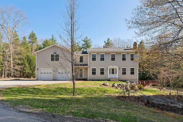 colonial-style house featuring an attached garage, a chimney, driveway, and a front yard