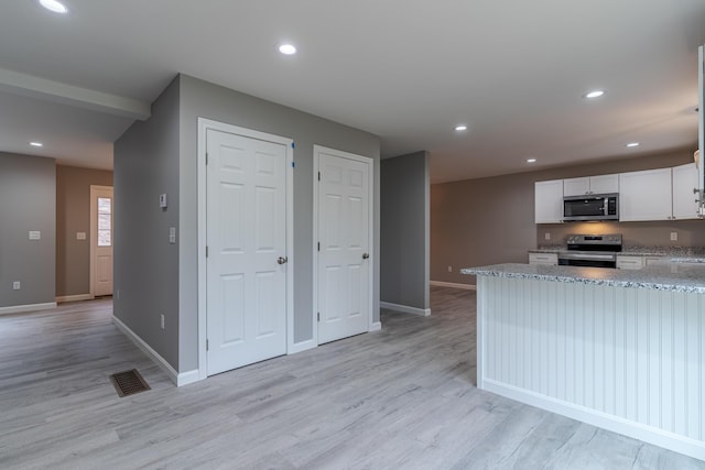 kitchen featuring light wood-style flooring, white cabinetry, light stone counters, and appliances with stainless steel finishes