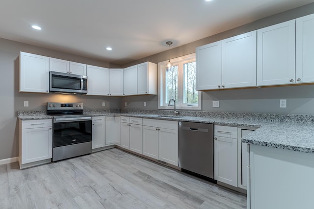 kitchen with a sink, stainless steel appliances, light wood-style floors, light stone counters, and recessed lighting