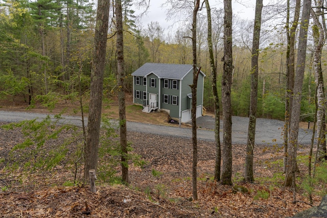 exterior space with roof with shingles, a view of trees, aphalt driveway, and an attached garage