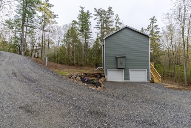 view of property exterior with gravel driveway, stairs, a view of trees, and an attached garage