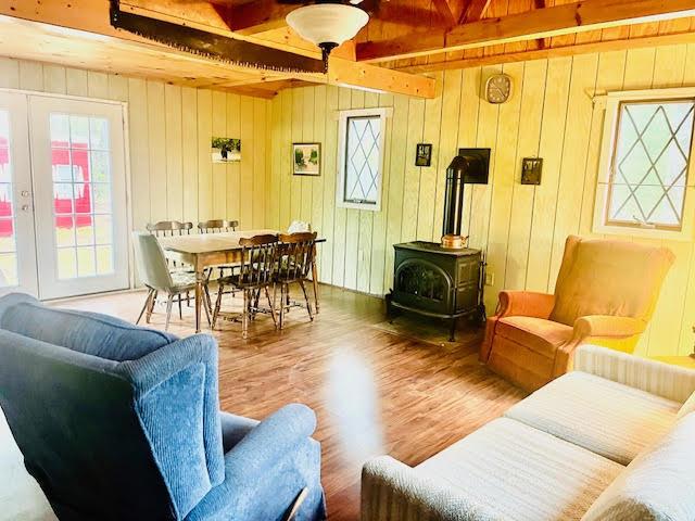 living area featuring wood finished floors, a wood stove, beam ceiling, and wooden walls