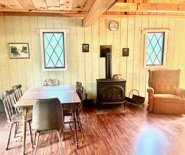 dining room featuring a wood stove, wood ceiling, wood finished floors, healthy amount of natural light, and wood walls