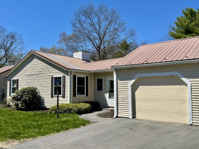 ranch-style house featuring a front lawn, aphalt driveway, a chimney, metal roof, and an attached garage