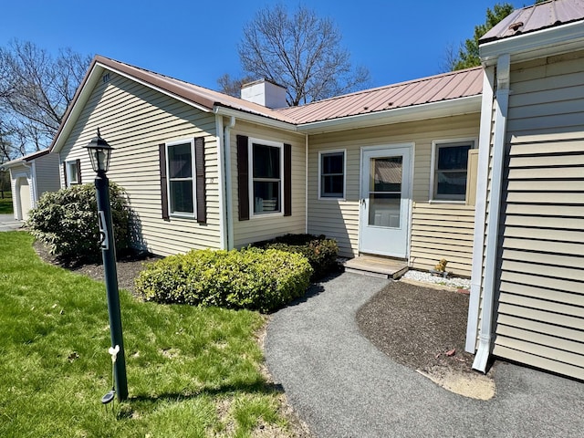 entrance to property with a yard, a chimney, and metal roof