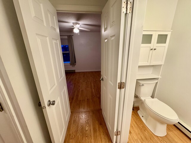 bathroom with a ceiling fan, wood finished floors, baseboards, a baseboard radiator, and toilet