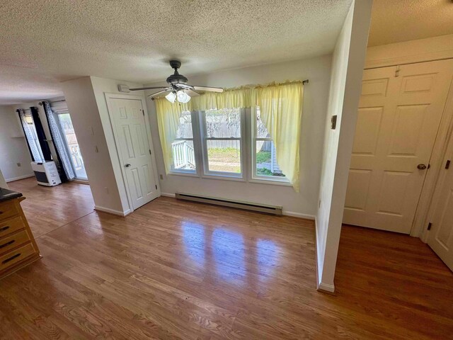 unfurnished dining area featuring baseboard heating, a ceiling fan, a textured ceiling, and wood finished floors