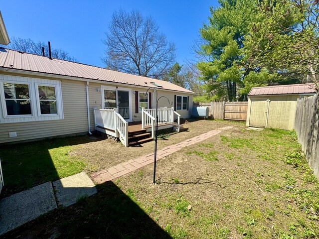 rear view of property with metal roof, a storage shed, a wooden deck, an outdoor structure, and a fenced backyard