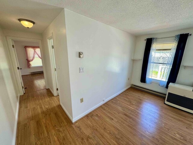 spare room featuring baseboards, a textured ceiling, wood finished floors, and a baseboard radiator