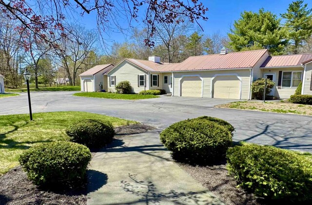 ranch-style home with an attached garage, a front lawn, a chimney, driveway, and metal roof