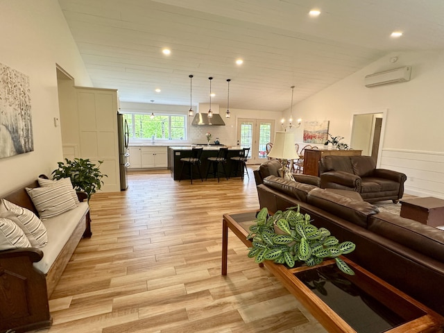living room featuring an AC wall unit, light wood-style flooring, vaulted ceiling, french doors, and a chandelier