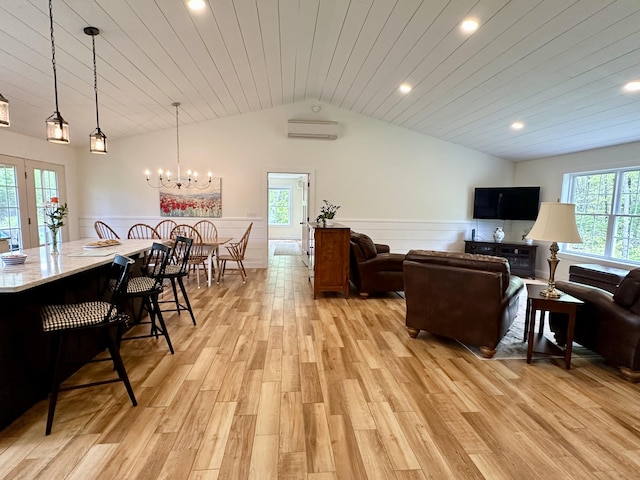 living area featuring vaulted ceiling, an AC wall unit, wainscoting, light wood-type flooring, and a chandelier