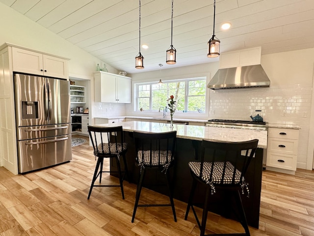 kitchen with stainless steel fridge, wall chimney range hood, white cabinets, decorative backsplash, and light wood-type flooring