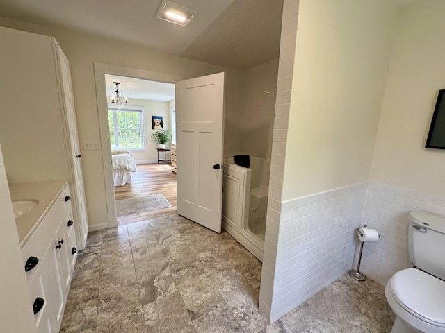 ensuite bathroom with toilet, a shower, vanity, wainscoting, and tile walls