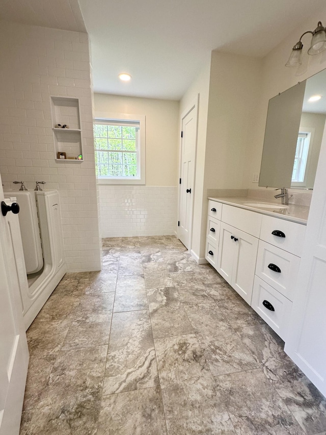 full bath with tile walls, vanity, and a wainscoted wall