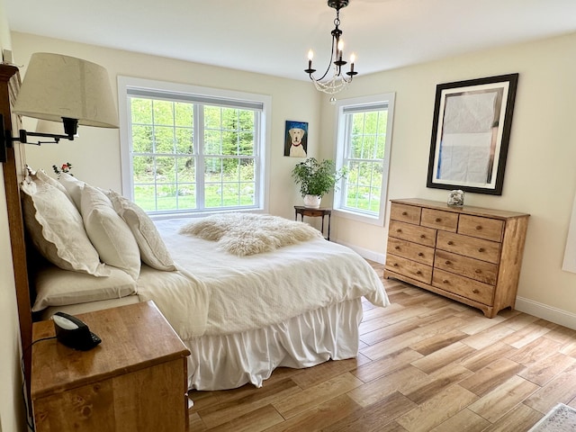 bedroom with a chandelier, light wood-type flooring, and baseboards