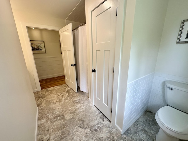 bathroom with toilet, a wainscoted wall, and a shower with curtain