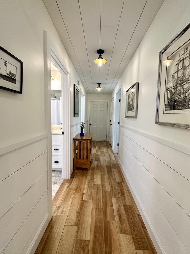 corridor featuring light wood-type flooring and wainscoting