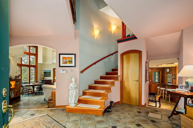 stairs featuring baseboards, arched walkways, and a high ceiling