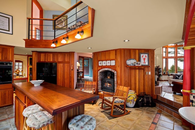 living area with a wood stove, recessed lighting, light tile patterned flooring, and a towering ceiling