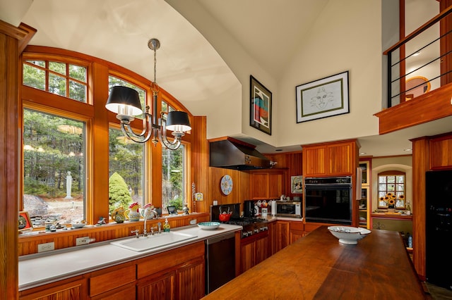 kitchen featuring exhaust hood, wooden counters, a sink, black appliances, and a notable chandelier