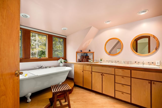full bathroom with double vanity, a freestanding bath, a sink, and wood finished floors