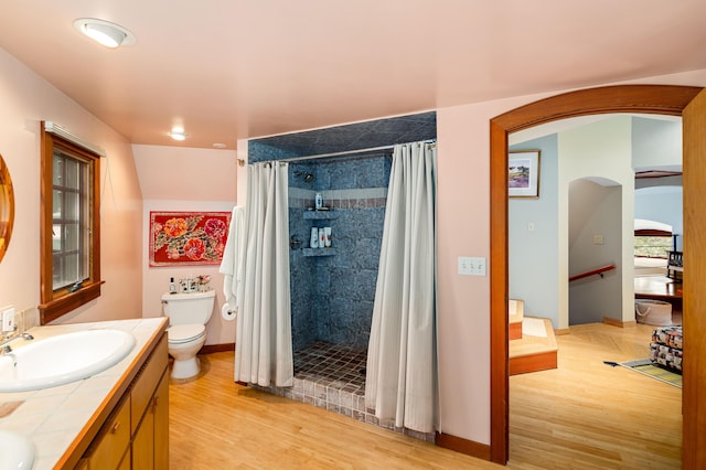 full bathroom featuring toilet, tiled shower, a sink, and wood finished floors