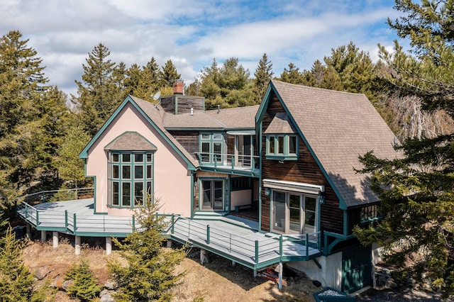 back of house featuring a shingled roof, a chimney, and a deck