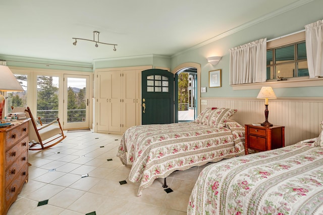 tiled bedroom featuring crown molding, arched walkways, access to outside, and a wainscoted wall