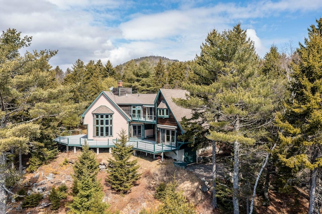 rear view of property featuring a view of trees, a wooden deck, a chimney, and a balcony