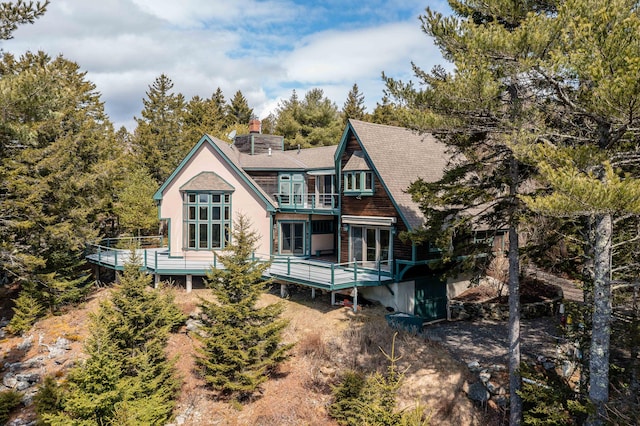 back of property featuring a shingled roof, a chimney, a deck, and a balcony