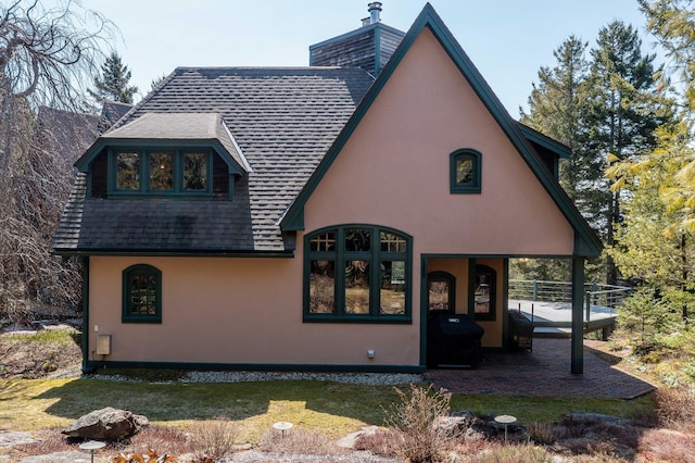 rear view of house featuring a shingled roof, stucco siding, a yard, and a chimney