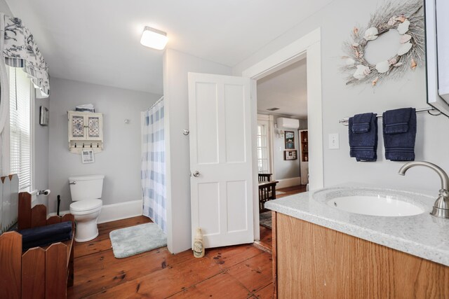 bathroom with hardwood / wood-style floors, a wall mounted air conditioner, toilet, vanity, and healthy amount of natural light