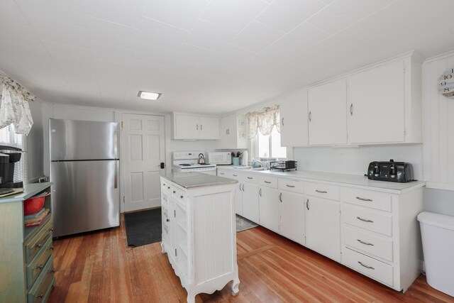 kitchen with freestanding refrigerator, white microwave, electric range oven, light wood-style floors, and white cabinetry