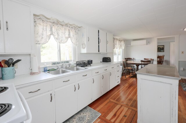kitchen with a sink, a wall mounted air conditioner, wood finished floors, and white cabinets