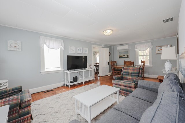 living area featuring an AC wall unit, wood finished floors, baseboards, and ornamental molding