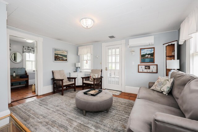 living room with a wall mounted AC, ornamental molding, baseboards, and wood finished floors