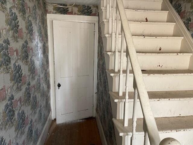 stairs with baseboards, wallpapered walls, and wood finished floors