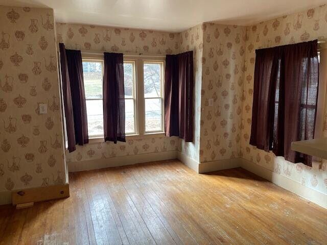 spare room featuring wallpapered walls, baseboards, and light wood finished floors