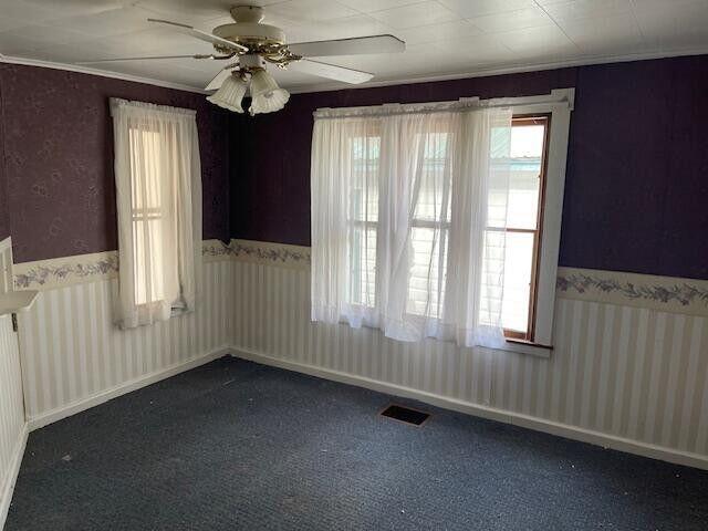 unfurnished room featuring ceiling fan, visible vents, a wainscoted wall, wallpapered walls, and dark carpet