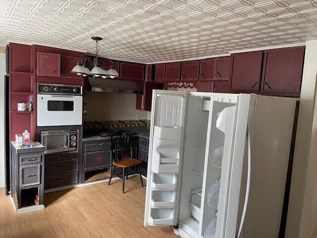 kitchen featuring light wood-style floors, an ornate ceiling, freestanding refrigerator, and pendant lighting